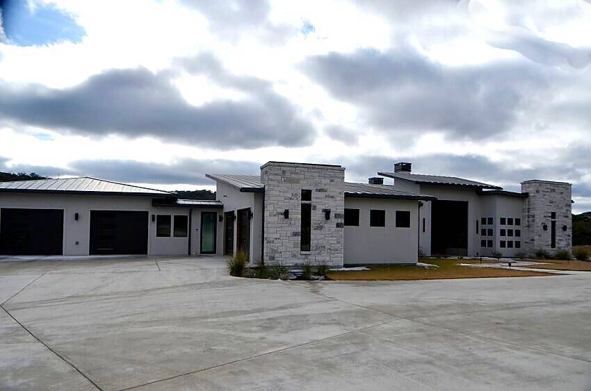Completed modern contemporary home exterior with white stucco, stone accents, and metal roof - Riverside Home Designs Custom Home Portfolio